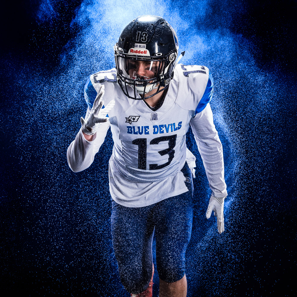 Studio-Sportportrait eines American Footballers der mit Ball auf die Kamera zu läuft